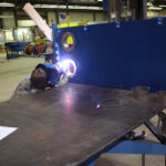 Welder welding metal port liners to fxd plate